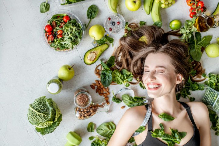 Uśmiechnięta kobieta leży wśród warzyw i owoców