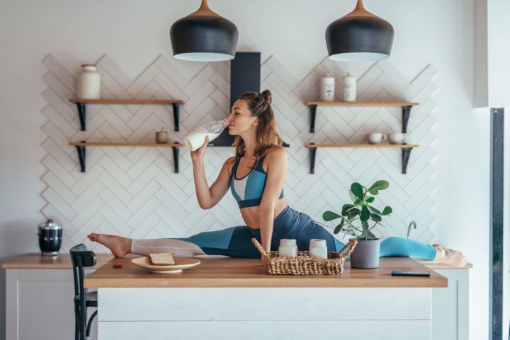Kobieta w stroju sportowym robi szpagat na blacie kuchennym pijąc mleko