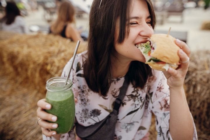 Uśmiechnięta kobieta zjada vegańskiego burgera